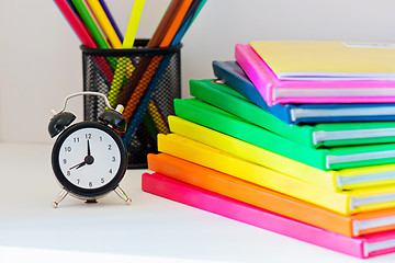 Image showing Black alarm clock. Multi colored books in stack