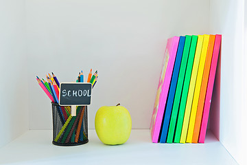 Image showing Yellow apple, pencils in holder and multi colored books 