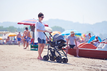 Image showing mother walking on beach and push baby carriage
