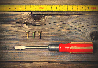 Image showing old screwdriver, three screws and measuring tape on textured boa