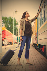 Image showing woman with luggage waves his hand near passenger railcar 