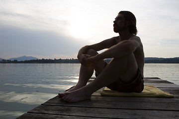 Image showing Young man sitting at a bridge in evening light