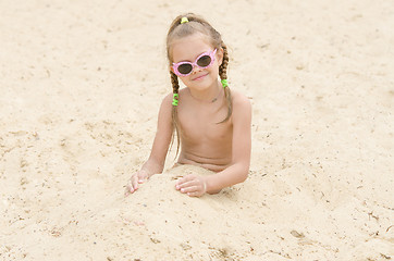 Image showing Five-year girl with glasses on beach covered with sand up to his waist