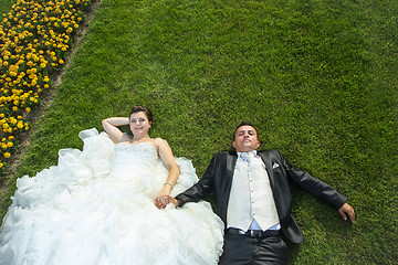 Image showing Bride and groom holding hands on lawn with flowers