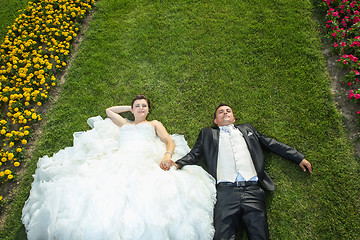Image showing Bride and groom lying on lawn with flowers