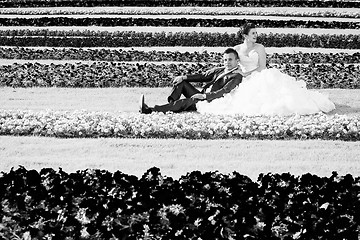 Image showing Bride and groom sitting on lawn with flowers bw