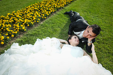 Image showing Newlyweds lying down on lawn with flowers