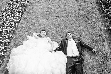 Image showing Bride and groom lying on lawn with flowers bw