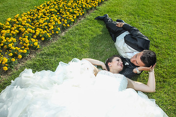 Image showing Bride and groom lying down on lawn with flowers