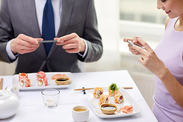 Image showing close up of couple with smartphones at restaurant