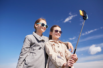 Image showing happy girls with smartphone selfie stick