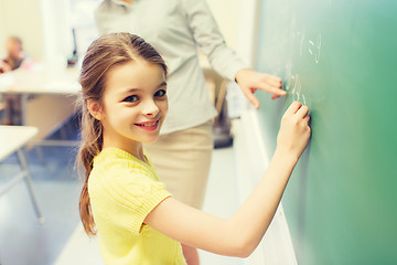 Image showing little smiling schoolgirl writing on chalk board