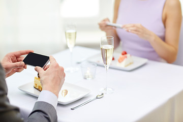 Image showing close up of couple with smartphones at restaurant