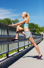 Image showing smiling woman stretching leg outdoors