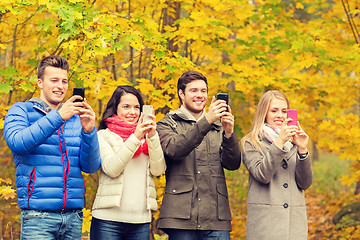 Image showing smiling friends with smartphones in city park