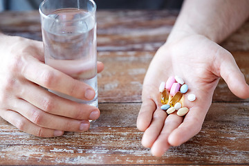 Image showing close up of male hands holding pills and water