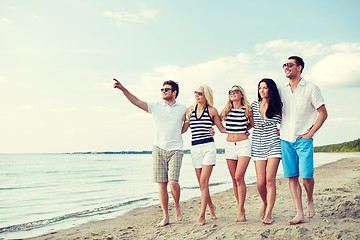 Image showing smiling friends in sunglasses walking on beach