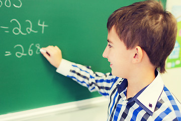 Image showing little smiling schoolboy writing on chalk board