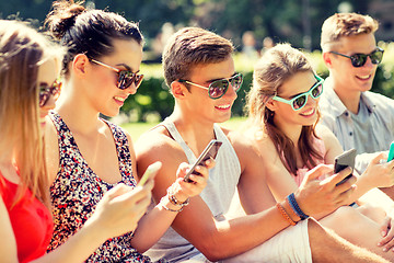 Image showing smiling friends with smartphones sitting on grass