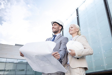 Image showing smiling businessmen with blueprint and helmets