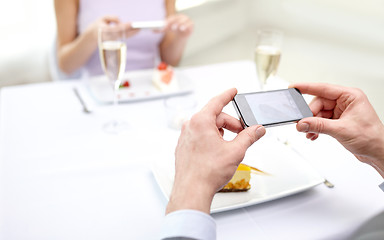 Image showing close up of couple with smartphones at restaurant