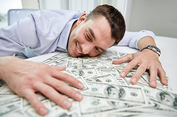 Image showing happy businessman with heap of money in office