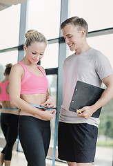 Image showing smiling young woman with personal trainer in gym