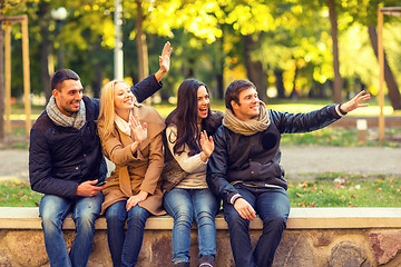 Image showing group of smiling friends waving hands in city park