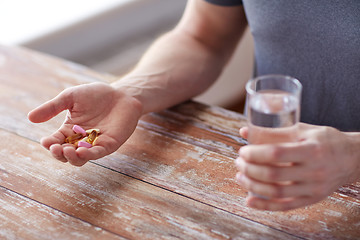 Image showing close up of male hands holding pills and water