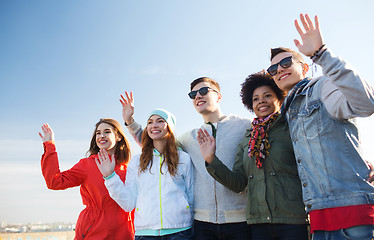 Image showing happy teenage friends in shades waving hands