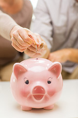 Image showing close up of hands putting coin money to piggy bank