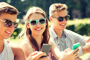 Image showing smiling friends with smartphones sitting in park