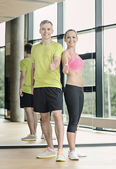 Image showing smiling man and woman showing thumbs up in gym