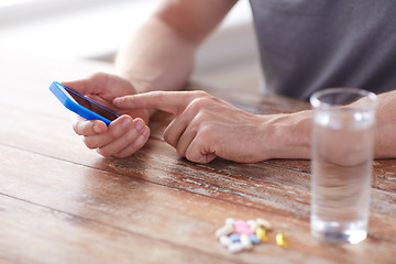 Image showing close up of hands with smartphone, pills and water