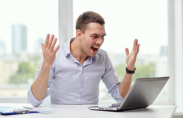 Image showing angry businessman with laptop and papers in office