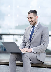 Image showing smiling businessman working with laptop outdoors