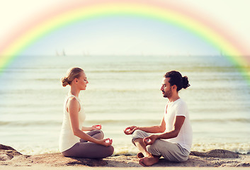 Image showing happy couple meditating in lotus pose on beach