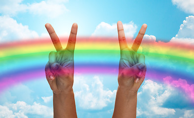 Image showing hands showing peace sign over rainbow in sky