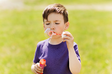 Image showing little boy blowing soap bubbles outdoors