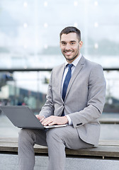 Image showing smiling businessman working with laptop outdoors