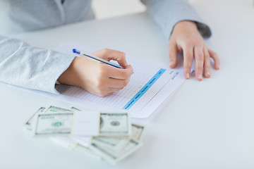 Image showing close up of hands with money filling tax form