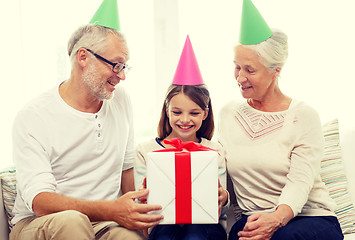 Image showing smiling family in party hats with gift box at home