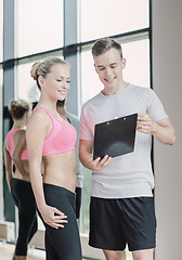 Image showing smiling young woman with personal trainer in gym