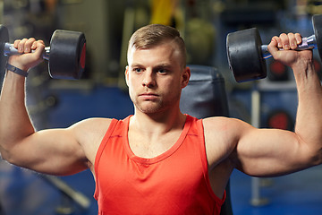 Image showing young man with dumbbells flexing muscles in gym