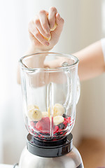 Image showing close up of woman hand adding fruits to blender