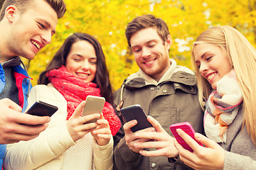 Image showing smiling friends with smartphones in autumn park