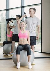 Image showing smiling young woman with personal trainer in gym