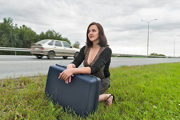 Image showing Beautiful woman with suitcase waits on road