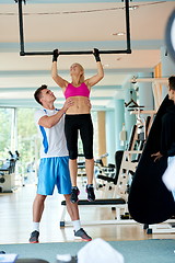 Image showing trainer support young woman while lifting on bar in fitness gym