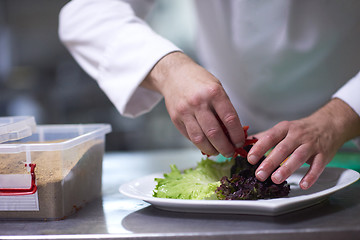 Image showing chef in hotel kitchen preparing and decorating food